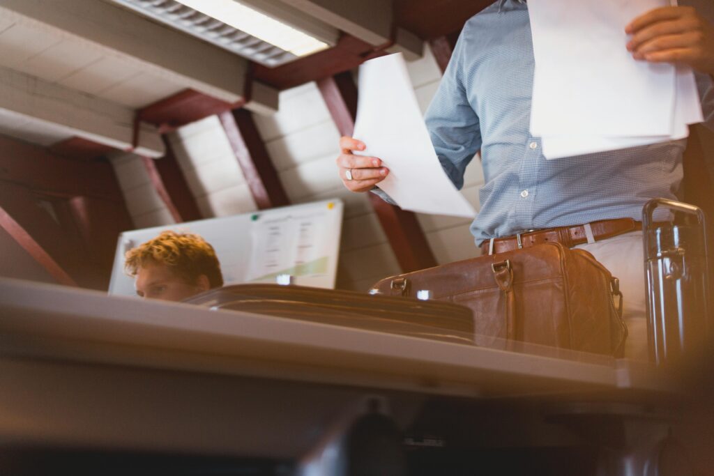 Startseite A businessman reviews documents with a leather bag in an office setting.