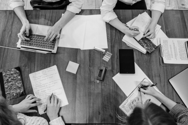 Startseite Top view of team members working together on a wooden table, using various office tools.